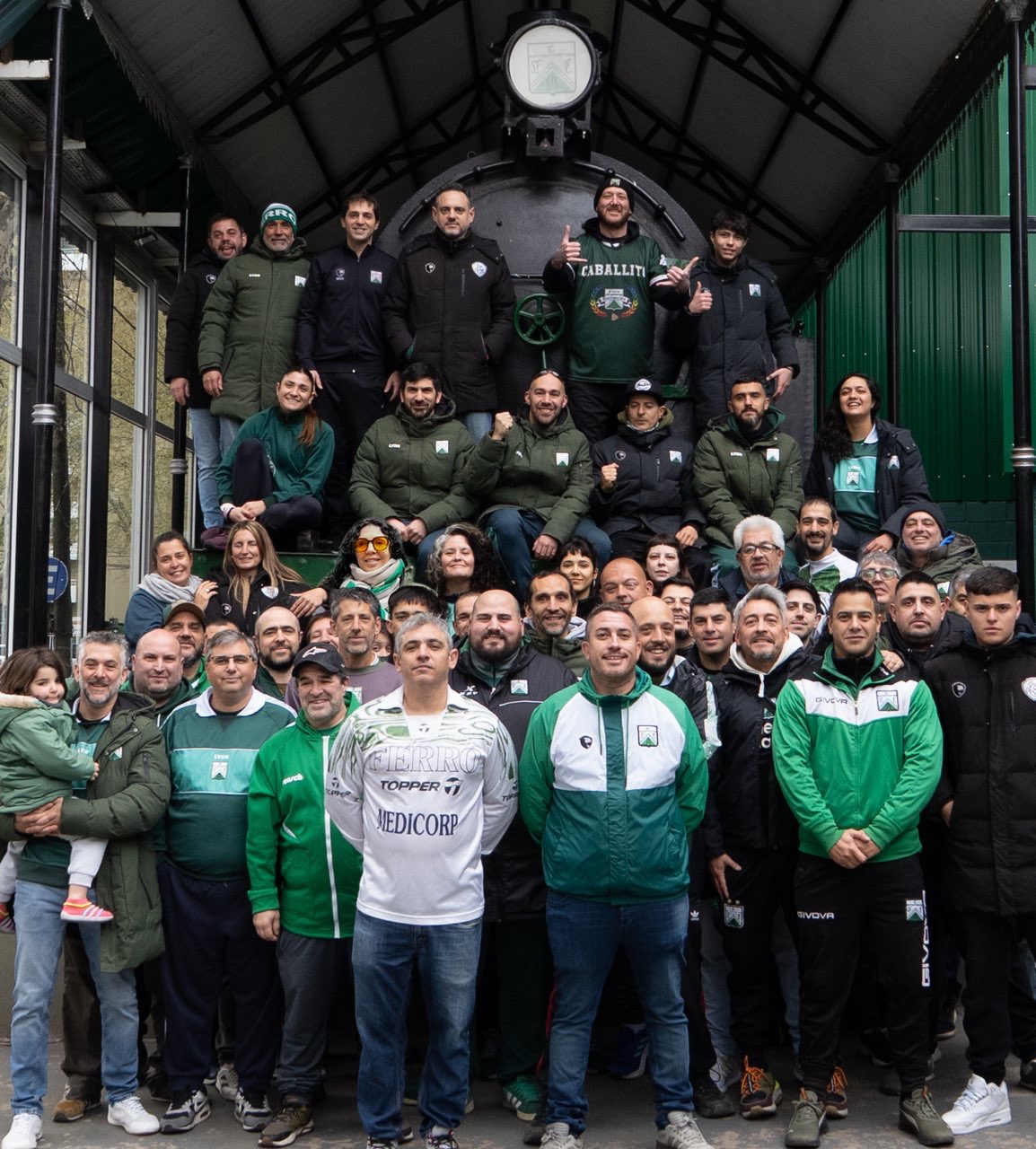 Socios y socias de Ferro en Acción reunidos junto a una locomotora del club